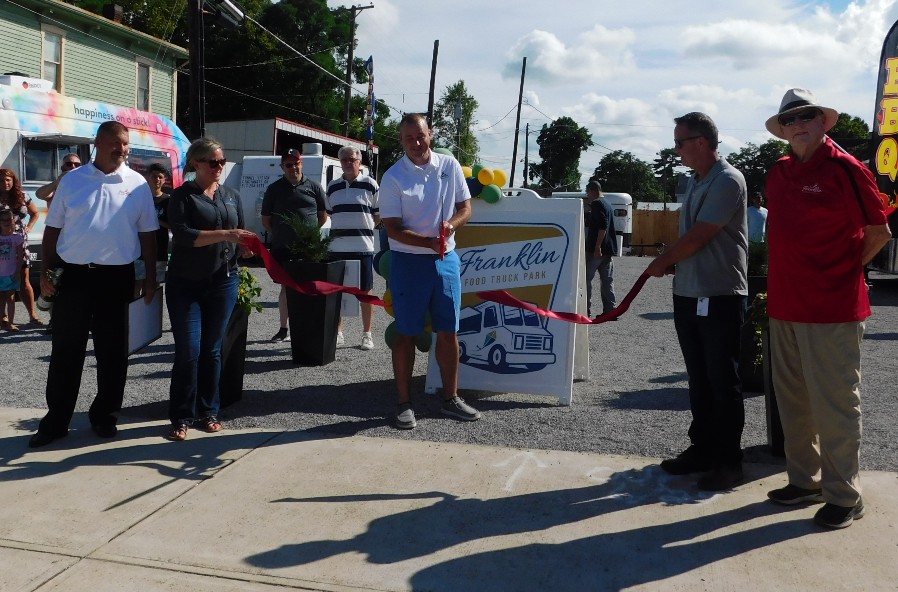 People using giant scissors to cut a red ribbon.